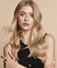 Blonde woman with long wavy hair wearing a black sleeveless top against beige background