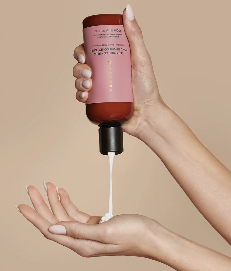 Ceramide Complex Bond Repair Conditioner in brown bottle with pink label dispensing white cream into hand