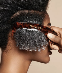Close-up of dark curly hair with white conditioner being combed using a brown Monpure wide-tooth comb