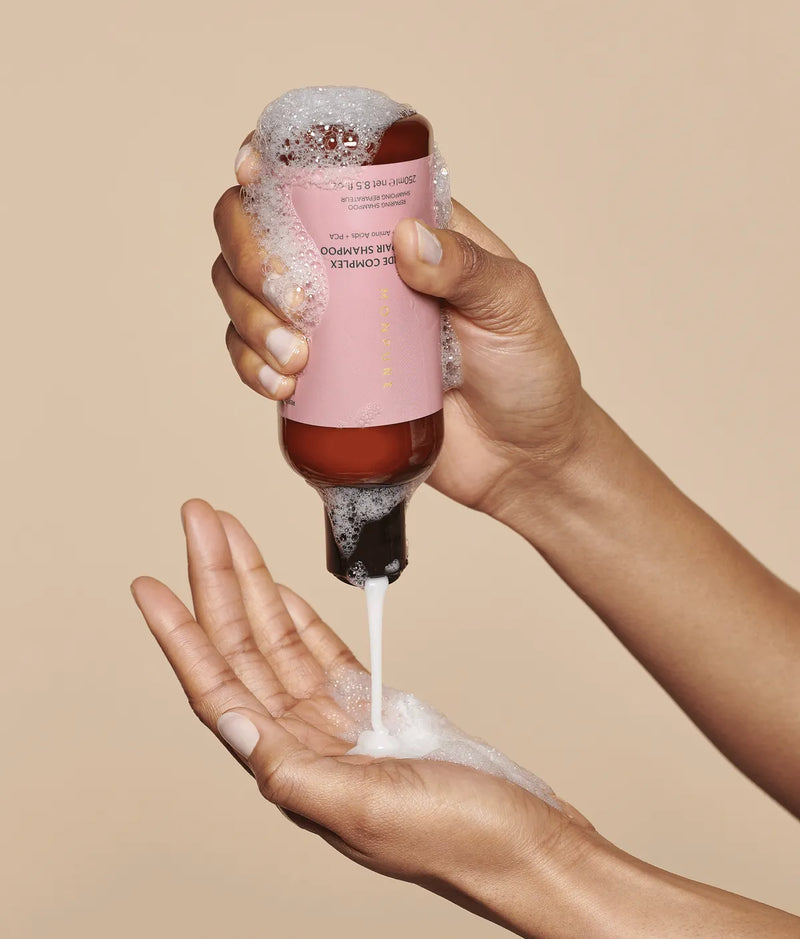 Hands dispensing white foamy Ceramide Complex Bond Repair Shampoo from brown bottle with pink label