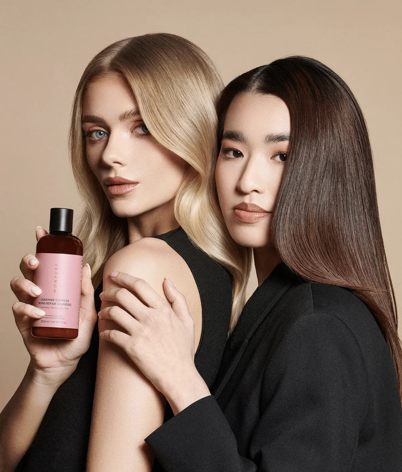 Ceramide Complex Bond Repair Shampoo in amber bottle with pink label held by woman with blonde hair, alongside woman with long dark hair