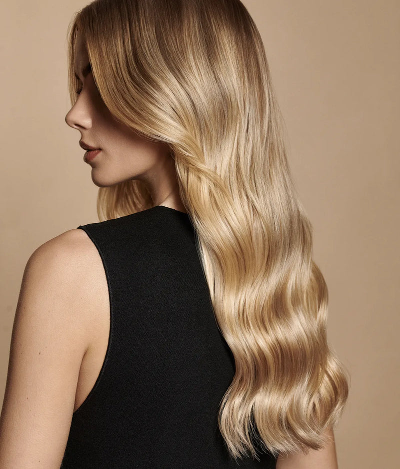 Woman with long, smooth, shiny blonde hair styled in loose waves wearing a black sleeveless top