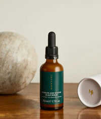 Amber glass bottle with black dropper containing Hydrate and Soothe Scalp Serum on wooden surface