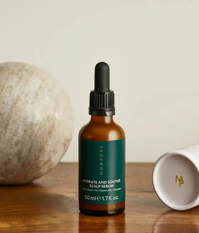 Amber glass bottle with black dropper containing Hydrate and Soothe Scalp Serum on wooden surface