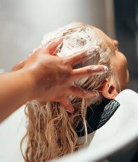 Blonde hair being shampooed with foamy lather at a salon wash basin for hair restoration