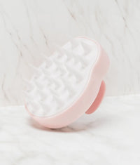 Pink and white silicone scalp massage brush with soft flexible bristles on marble surface