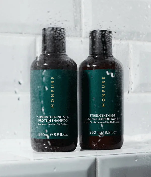 Two dark brown bottles of Monpure strengthening shampoo and conditioner with green labels on white tiled surface