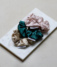 Trio of silk scrunchies in beige, dark green, and pale pink on a white marble slab