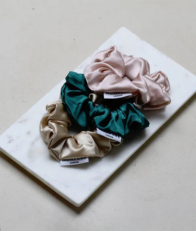 Trio of silk scrunchies in beige, dark green, and pale pink on a white marble slab