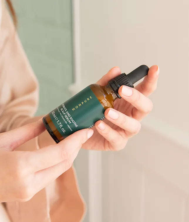 Amber glass dropper bottle with dark green label held by hands, skincare serum product